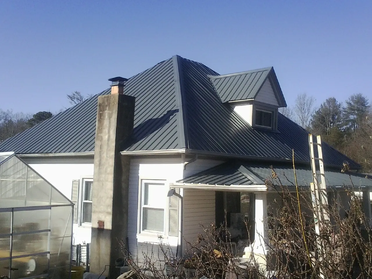 Dark blue standing seam metal roof on a white farmhouse with dormer in Zolfo Springs