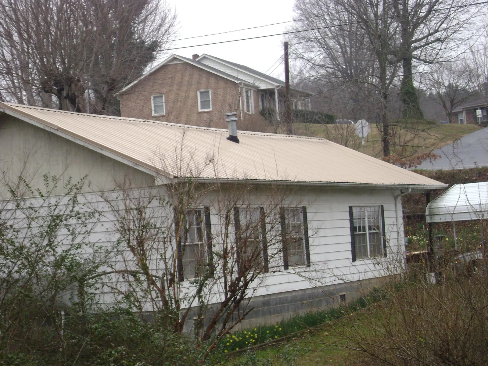 Tan metal roof on a white sided house set into a hillside — Commercial Roofing by Roofing Brothers in Zolfo Springs